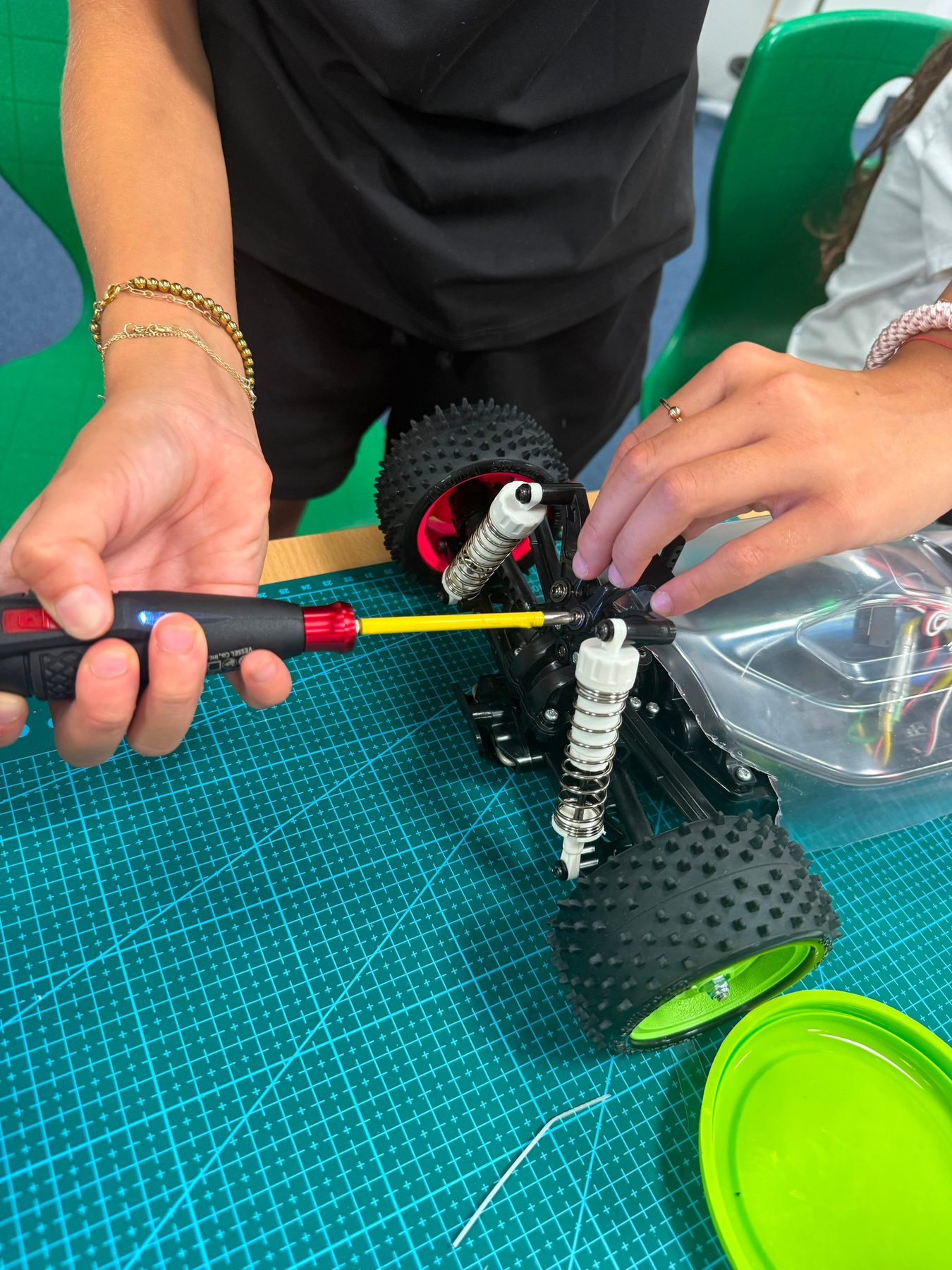 Two participants fitting suspension parts to an RC buggy chassis with an electric screwdriver